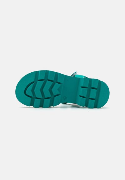 Turkos sandal med en texturerad gummisula som har ett zickzackmönster och justerbart rem. Slätt ovanmateriel, minimal detaljering.