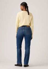 Ανοιχτόκίτρινο πουλόβερ με πλέξη cable και ψηλόμεσο μπλε τζιν με δύο πίσω τσέπες. Σκούρα παπούτσια ολοκληρώνουν την εμφάνιση.