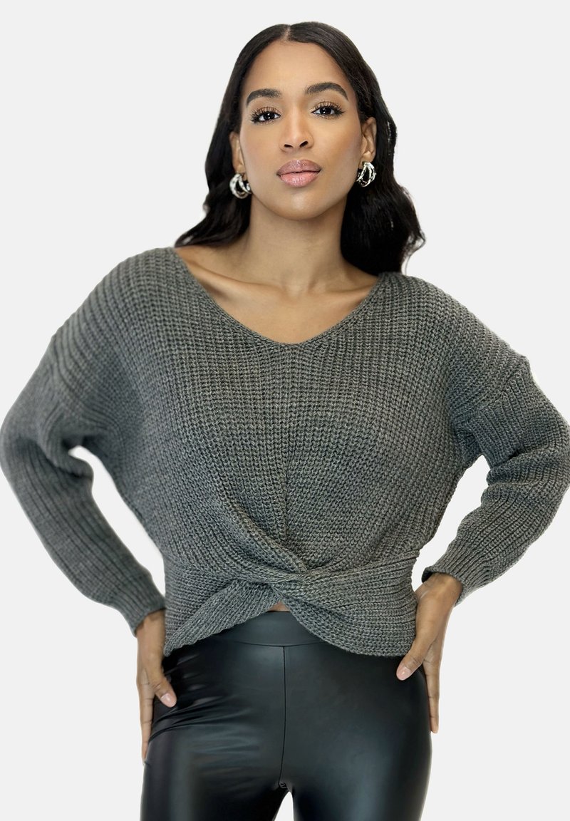 Grauer gestrickter Pullover mit weitem V-Ausschnitt, strukturiertem Stoff und geknotetem Frontdetail, kombiniert mit schwarzen Leggings.