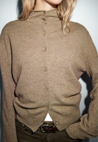 Brown ribbed cardigan with a high collar, featuring five buttons and a slightly tapered shape. Soft texture, casual fit, and lightweight material.