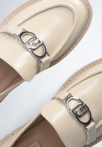 Mocassini beige in pelle con fibbia metallica, punta rotonda e cuciture a contrasto lungo la suola, caratterizzati da una superficie liscia e lucida.