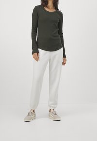 Långärmad, mörkgrön ribbad topp med rundad halsringning, kombinerad med vita joggers med elastiska kh cuffar och beige sneakers med ränder.