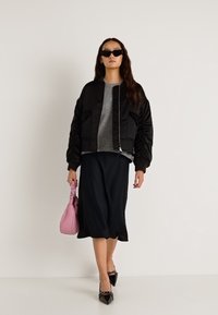 Sort bomberjakke med quiltede ærmer, grå sweater, sort nederdel, lyserød håndtaske, sorte spidse flade sko, solbriller, tekstureret stof.