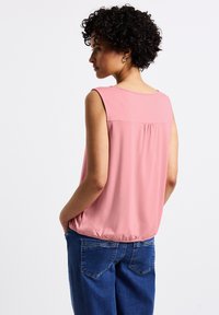 Rosa utan ärmar blus med rundad halsringning, texturerad ok och samlad bakdetalj, i kombination med blå denimbyxor.