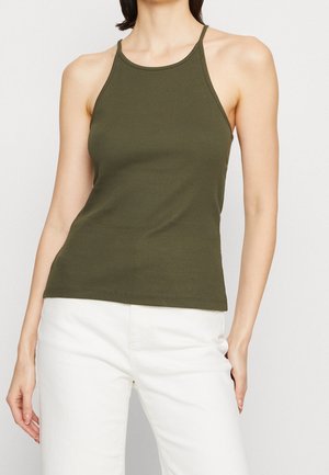 Débardeur côtelé vert olive avec un col montant et de fines bretelles spaghetti. Le tissu est léger et ajusté, associé à un pantalon blanc.