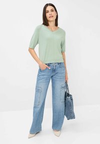 Helles grünes Kurzarmoberteil kombiniert mit weiten blauen Jeans mit Cargo-Taschen und einer Jeans-Tasche. Glatter Stoff und lässiges Design.
