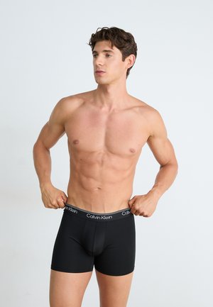 Zwarte Calvin Klein boxershorts met een logoband, een aansluitend ontwerp, een gladde textuur en een lengte tot halverwege de dij, gepresenteerd op een shirtloze mannelijke model.