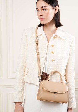 Sac à main en cuir tan au design structuré, avec une poignée supérieure, une bandoulière réglable et une fermeture magnétique. Porté avec une veste crème texturée.