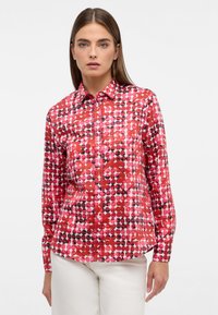 Rotes Hemd mit Knopfleiste und einem gepunkteten Muster in verschiedenen Schattierungen von Pink und Schwarz. Hergestellt aus glattem Stoff, hat es lange Ärmel und einen klassischen Kragen.