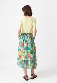 Lichtgroene top met korte mouwen gecombineerd met een midi-lange, kleurrijke, gestreepte rok met geometrische vormen in turquoise, rood en geel.