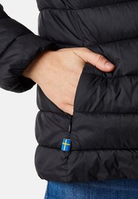 Giubbotto puffer nero con design trapuntato. Presenta una tasca con zip e un piccolo accento della bandiera svedese vicino all'orlo. Texture morbida e liscia.