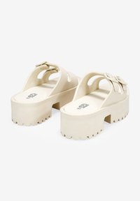 Sandali platform crema con dettagli traforati e una fibbia prominente. Suola texturizzata con bordi frastagliati per una migliore aderenza.
