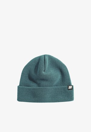 Strickmütze in Türkis mit umgeschlagenem Bund und einem kleinen schwarzen Etikett mit weißem Logo. Der Stoff wirkt weich mit einer gerippten Textur.