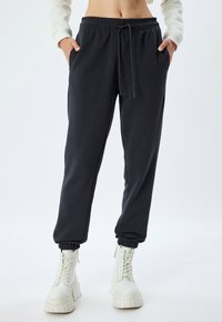 Mørkegrå sweatpants lavet af blødt materiale med elastisk talje, snor og elastiske ankelmanchetter. Lommer på hver side.