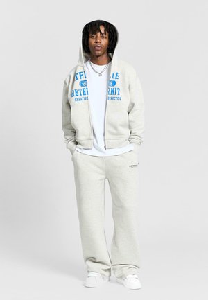 Šedá mikina s modrým potiskem, spárovaná se šedými tepláky. Materiál je měkký, casual design s předním zipem a kapsami.