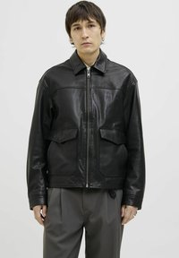 Jachetă din pielă neagră cu fermoar pe față, guler ascuțit, două buzunare frontale aplicate și o textură netedă, lucioasă. Croială casual și design modern.
