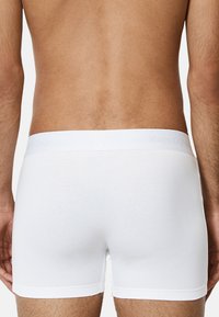 Boxers en coton blanc avec une texture lisse, ornés d'un logo discret sur la ceinture élastique et d'un design ajusté.