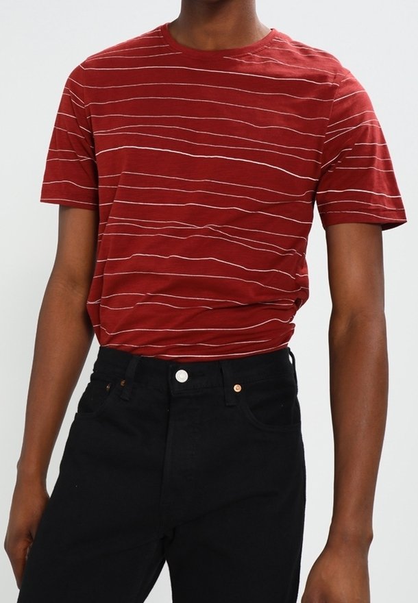 Punainen raidallinen t-paita kevyestä kankaasta, jossa on lyhyet hihat, yhdistettynä mustiin farkkuihin, joissa on klassinen muotoilu ja nappiyksityiskohtia.