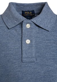 Polo tričko v tmavě modré texturované tkanině s klasickým límečkem, na němž jsou dva bílé knoflíky a štítek s nápisem "Polo Ralph Lauren."