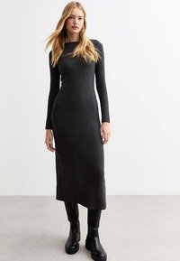 Langsleeve, rib gebreid jurk in donkergrijs, met een aansluitende silhouet en ronde halslijn. Gecombineerd met zwarte enkellaarsjes.