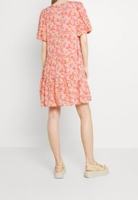 Fliederfarbenes Kleid mit Puffärmeln, gestuftem Rock und weicher Textur. Kombiniert mit beigen Plateausandalen mit gelben Riemen.