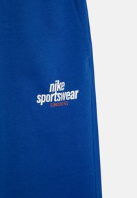 Modre bombažne kratke hlače z belim logotipom Nike Sportswear in napisem "ESTABLISHED 1972" v oranžni barvi. Gladka tekstura z ohlapnim krojem.