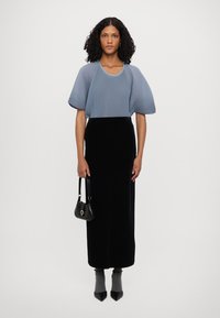 Helles blaues, plissiertes Top mit kurzen, puffärmeligen Ärmeln; schwarze, figurbetonte Samt-Rock; graue Socken; schwarze spitz zulaufende Schuhe; kleine schwarze Handtasche.