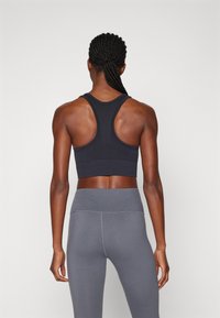 Sostén deportivo negro con diseño de espalda tipo nadador. Leggings grises de talle alto que ofrecen una textura suave y elástica. Sin patrones notables ni accesorios.