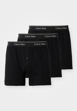 Trīs melnu kokvilnas bokseru pāri ar pogu, ar melnu jostu, uz kuras ir balta "Calvin Klein" uzraksts.