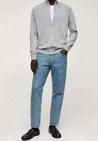 Cardigan grigio con zip, maglietta bianca a girocollo, jeans azzurri chiari e mocassini neri. Tessuto morbido, vestibilità rilassata e stile casual.