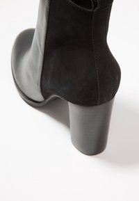 Botín negro de piel con textura suave, que presenta un tacón cilíndrico grueso y costuras a tono a lo largo de las costuras laterales.