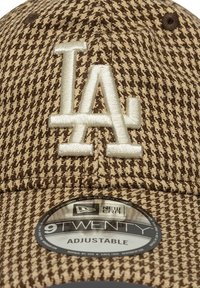 Bruin en beige geblokte baseballpet met geborduurd "LA" logo, verstelbare band en New Era label aan de onderkant van de klep.
