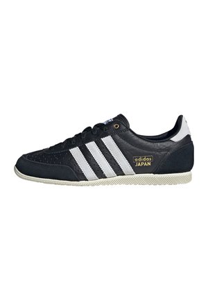 Czarny sneaker Adidas Japan z białymi paskami, złotym logo, czarnymi sznurowadłami i fakturowaną białą gumową podeszwą widoczny z profilu bocznego.