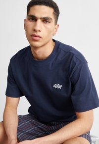 Marineblå kortærmet T-shirt lavet af bomuld, med et lille hvidt logo på brystet. Løs pasform med en klassisk rund halsudskæring.