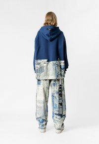 Sudadera de gran tamaño en color marino con una tela azul estampada en la parte inferior, combinada con pantalones de pierna ancha que presentan un patrón azul desgastado y una etiqueta.