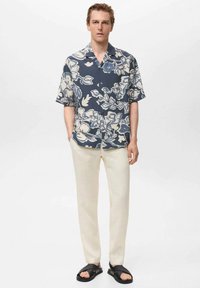 Korte mouwen marineblauw shirt met wit bloemenpatroon, crèmekleurige broek en zwarte instapsandalen. Relaxte pasvorm, knoopsluiting en kraagontwerp.