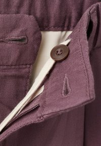 Gros plan sur un bouton en tissu violet et une boutonnière sur un vêtement, avec une doublure blanche visible en dessous.