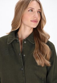 Zielona kurtka dżinsowa z zapięciem na guziki, kołnierzem i teksturowanym materiałem. Posiada delikatny haft na piersi i srebrne guziki.