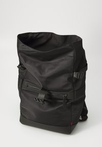 Zaino nero realizzato in materiale resistente, con design a chiusura roll-top, spallacci regolabili e tasca frontale con zip e dettagli in metallo.