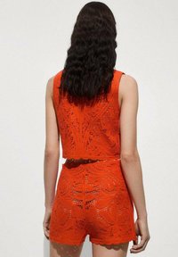 Helle orange gehäkelte Zweiteiler, bestehend aus einem kurzen Tanktop und hoch taillierten Shorts mit einem Blumenmuster und gewellten Kanten.