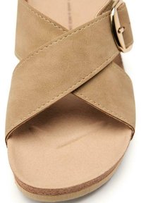 Sandalia de ante beige con tiras cruzadas y hebilla en tono dorado. Presenta una suela plana y un interior suave y liso.