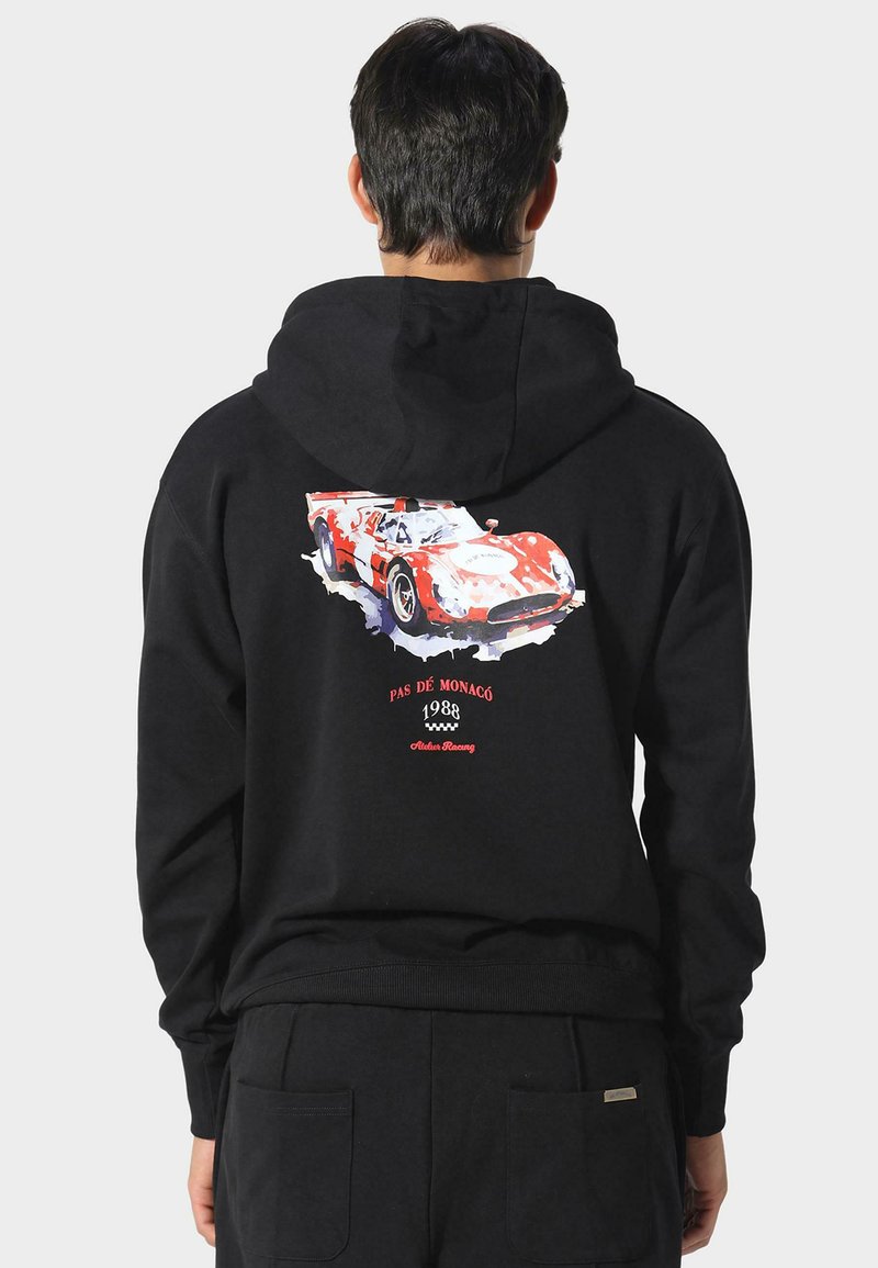 Sudadera negra con un gráfico colorido de un coche de carreras en la parte posterior, con el texto "PAS DE MONACO 1988" y "Arden Racing" debajo del diseño.