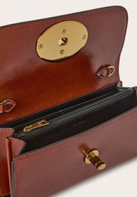 Borsa a tracolla in pelle marrone con accenti dorati. Presenta una chiusura metallica arrotondata e un interno foderato in nero con tasca con zip.