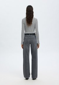 Camisola de manga longa às riscas em preto e branco, combinada com jeans de ganga cinza de perna larga e cintura alta. Apresenta dois bolsos traseiros e um cinto simples.