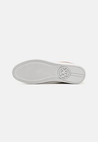 Suola di sneaker bianca con superficie in gomma testurizzata, logo circolare sul tallone e scanalature delicate per la trazione.
