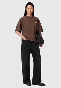 Camiseta de algodón marrón con mangas cortas y cuello redondo, combinada con jeans de pierna ancha negros de talle alto y planos negros.