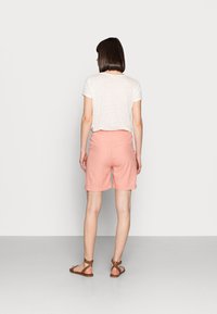 Shorts en lin rose avec une coupe décontractée, dotés de poches arrière et d'une texture douce, associés à un t-shirt blanc et des sandales marron.