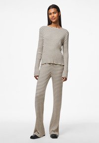 Langermet, ribbet loungewear-set med beige og svarte striper. Toppen har en avslappet passform med en asymmetrisk kant; buksene er utsvingte.