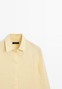 Chemise jaune clair à manches longues avec col et boutons, fabriquée en tissu texturé, présentée sur fond blanc.