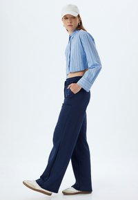 Korte blauwe gestreepte blouse met kraag, gecombineerd met losse marineblauwe joggingbroek. Witte pet en witte sneakers maken de look compleet.